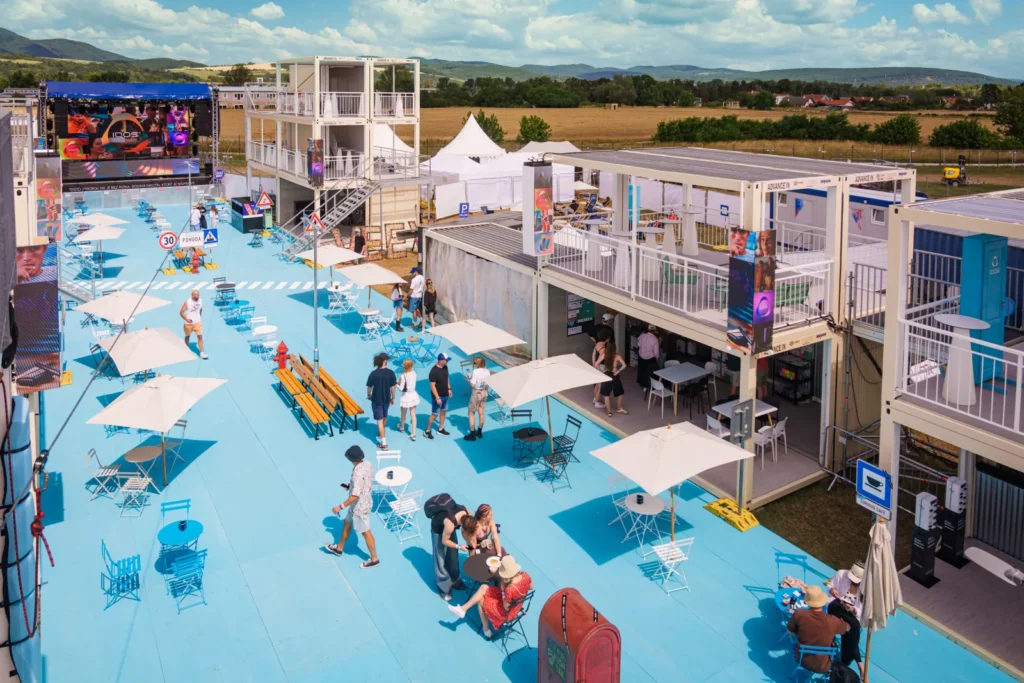 Letecký pohľad na zónu IQOS Curious City na Pohode – modrá festivalová ulica so slnečníkmi, kontajnermi a pódiom, v pozadí Malé Karpaty