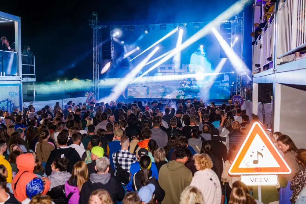 Nočný koncert v IQOS Curious City na Pohode s modrými lasermi a LED obrazovkou Curious City, dopravná značka VEEV v popredí