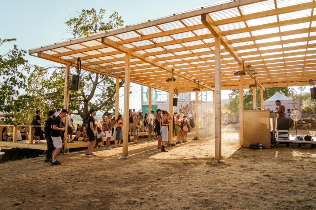 Drevené pódium pod pergolou v zóne IQOS Curious City s davom počas dňa na festivale Ženy Víno Funk