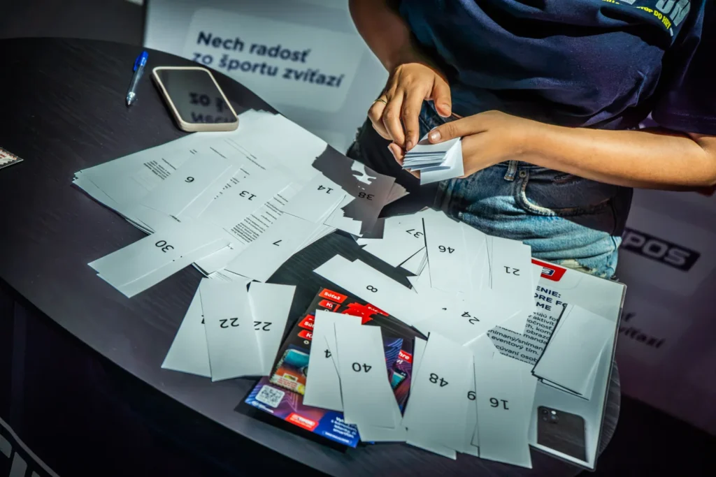 Rozložené hracie lístky s číslami a žreby Tipos The Game na registračnom stole počas huntu